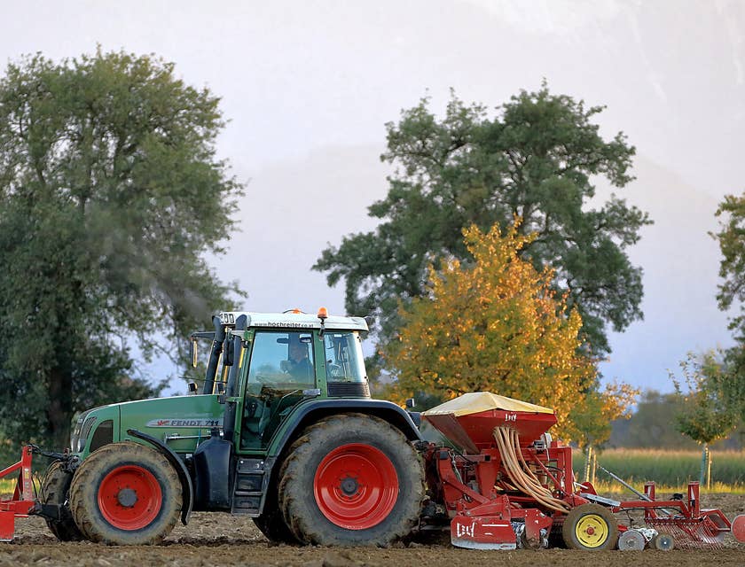 Una granja con tractor y otros equipos agrícolas con un empleado contratado por una bolsa de trabajo para agricultura.