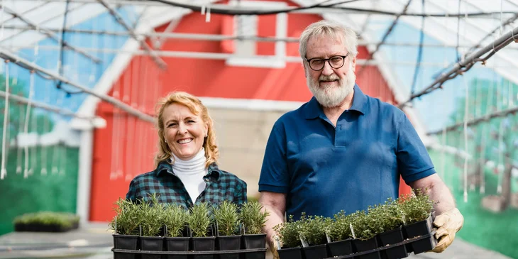 An elderly man and woman holding plants.