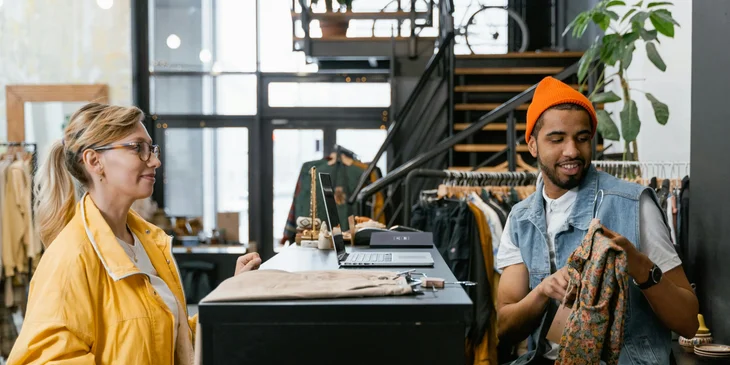 A man working in a clothing store assisting a customer.