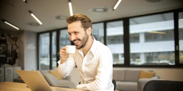 A man sitting on a chair while holding a cup in front of a table.