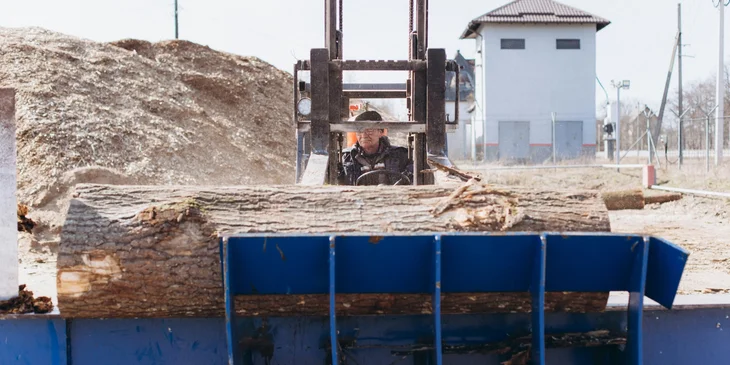 A man operating a tractor with a tree trunk in tow.