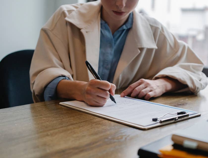 Una mujer en un abrigo beige llenando un formulario de solicitud de trabajo.