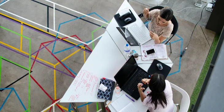 Coworkers engaged in a conversation at their table in the office space.