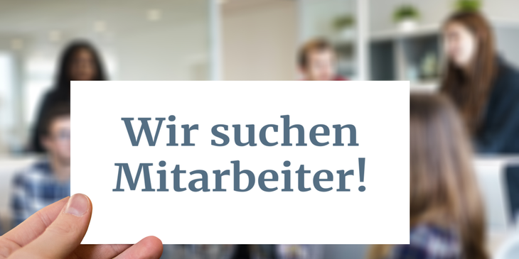 Ein Arbeitgeber hält ein Schild mit der Aufschrift „Wir stellen ein“ in englischer Sprache hoch.