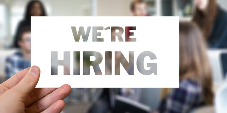 An employer holding up a sign that says "We're Hiring."