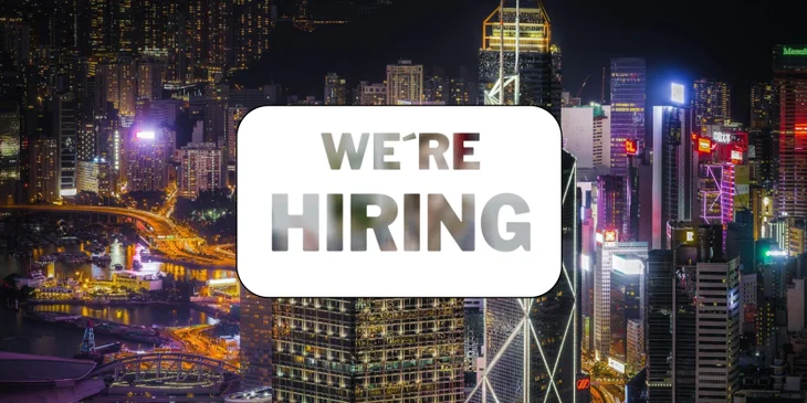 A sign that says "We're Hiring" in front of the Hong Kong skyline.