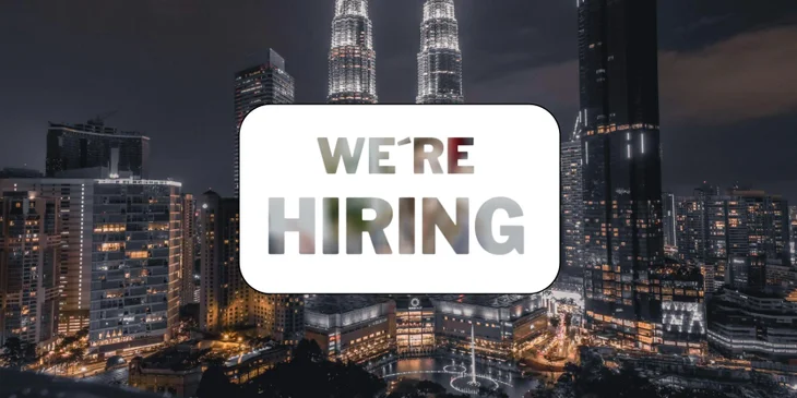 A sign that says "We're Hiring" in front of the Malaysia skyline.