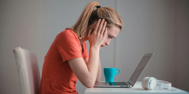A woman looking at her laptop with her head in her hands.