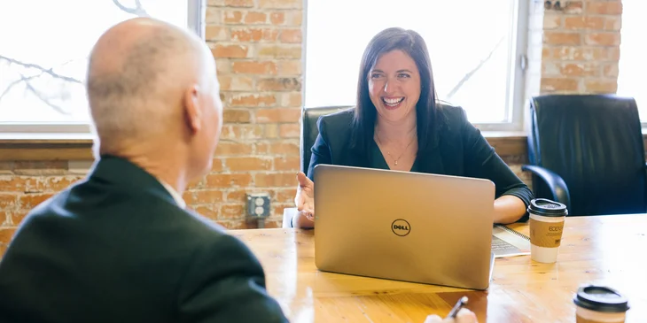 A woman talking to her coworker while working on her laptop.