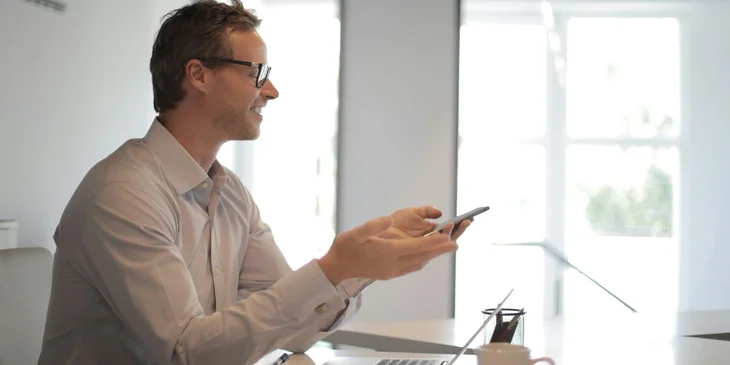 A smiling businessman at a table holding a mobile phone.