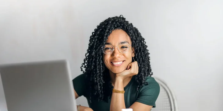 A happy woman sitting at a table with a laptop.