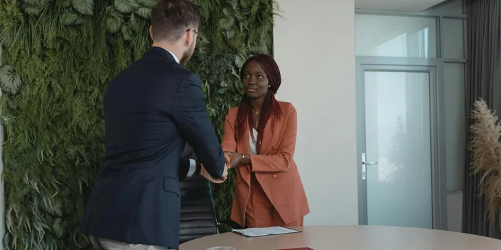 A newly hired employee shakes hands with the HR representative.