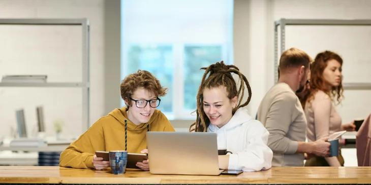 Two women working side by side on a laptop.
