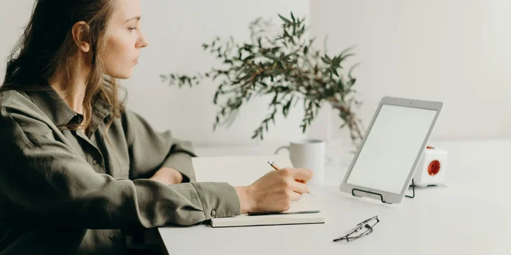 A woman working on her tablet while taking notes.