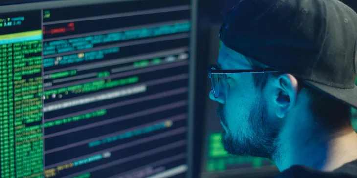 A man wearing eyeglasses typing code into a computer.