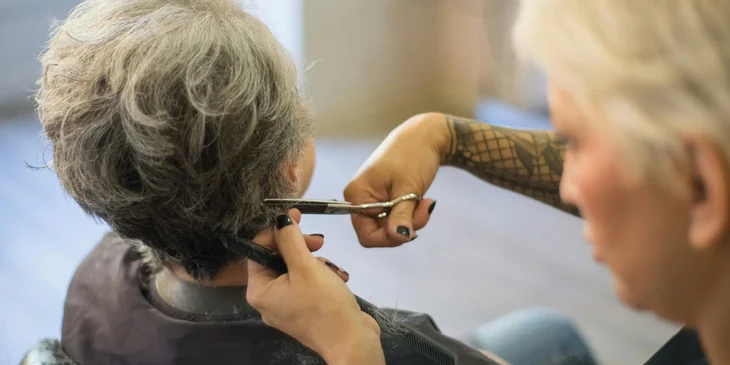 A hairstylist cutting an elderly woman's hair.