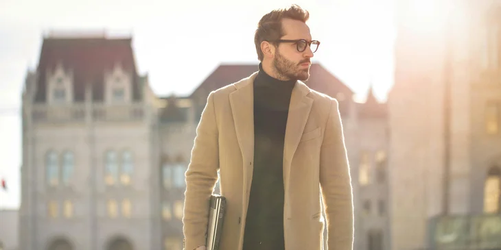 A man walking outdoors in the early morning while carrying a laptop.