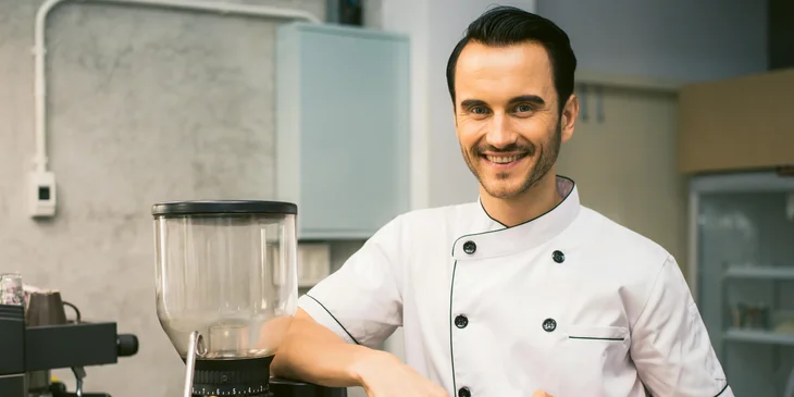 A head cook smiling next to a coffee machine.