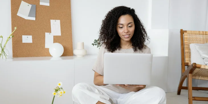 A woman sitting on the floor, using her laptop.