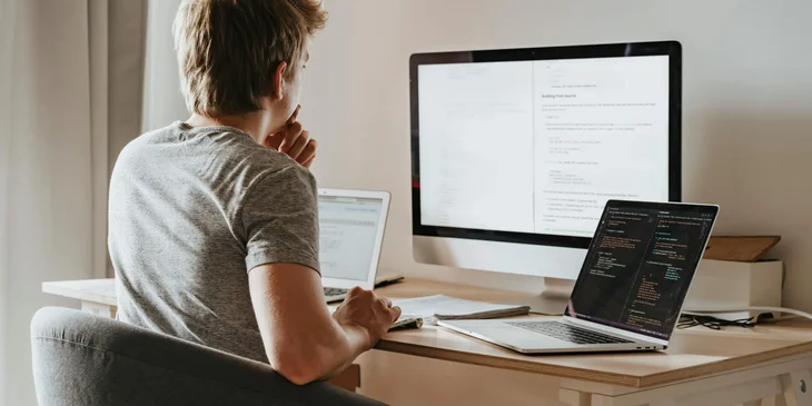 A man working on a coding program using three computers.