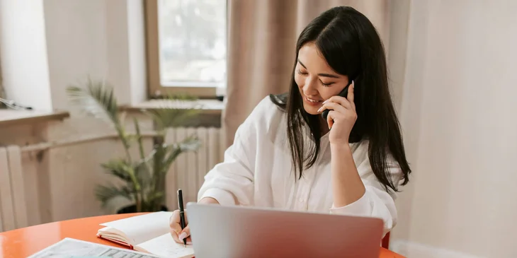 A woman talking on the phone while writing down notes.