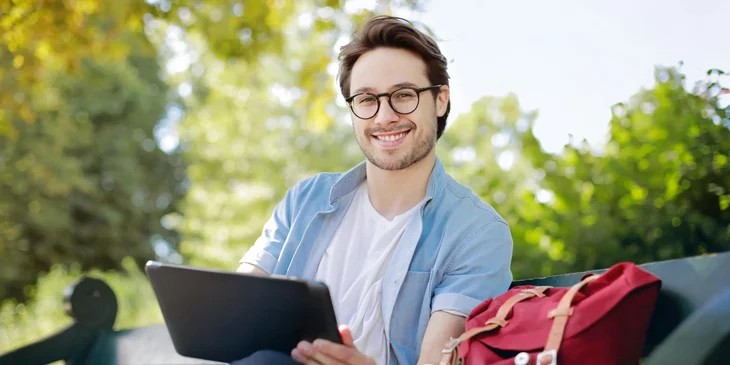 A man in a blue polo shirt using his tablet outdoors.