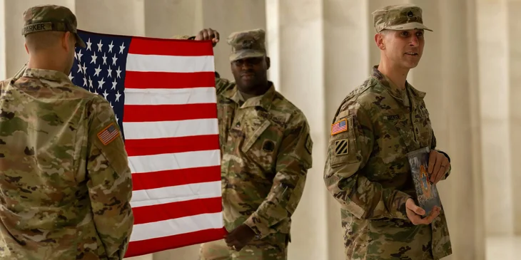 Two soldiers holding the American flag, while another soldier holds a short introduction to the program.