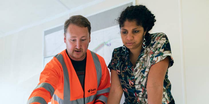 Two civil engineers scrutinizing blueprints on a table.