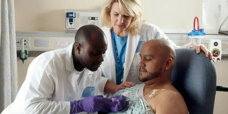 An assistant nurse looking on as nurse administers medication to a patient.