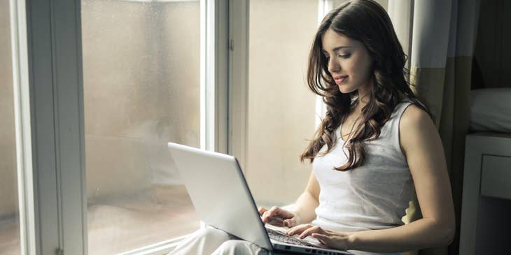 Woman sitting by the window and preparing an ats resume on her laptop