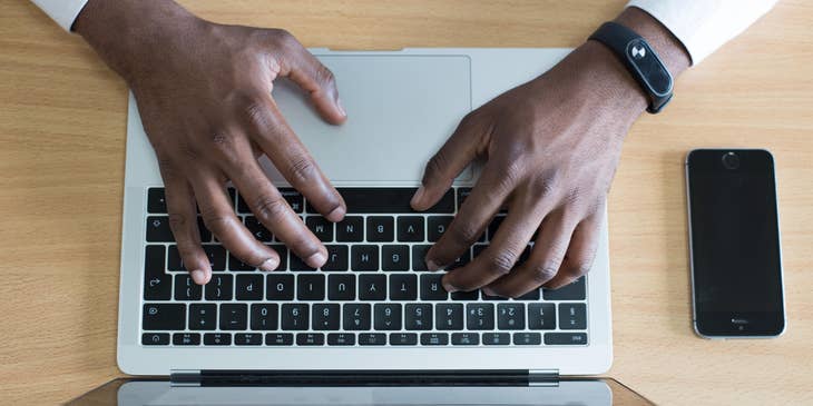 Person's hands on a MacBook writing a job description with an iPhone next to them.