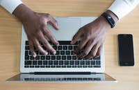 Eine Person tippt eine Stellenbeschreibung in einen Laptop ein und hat ein Mobiltelefon daneben liegen..