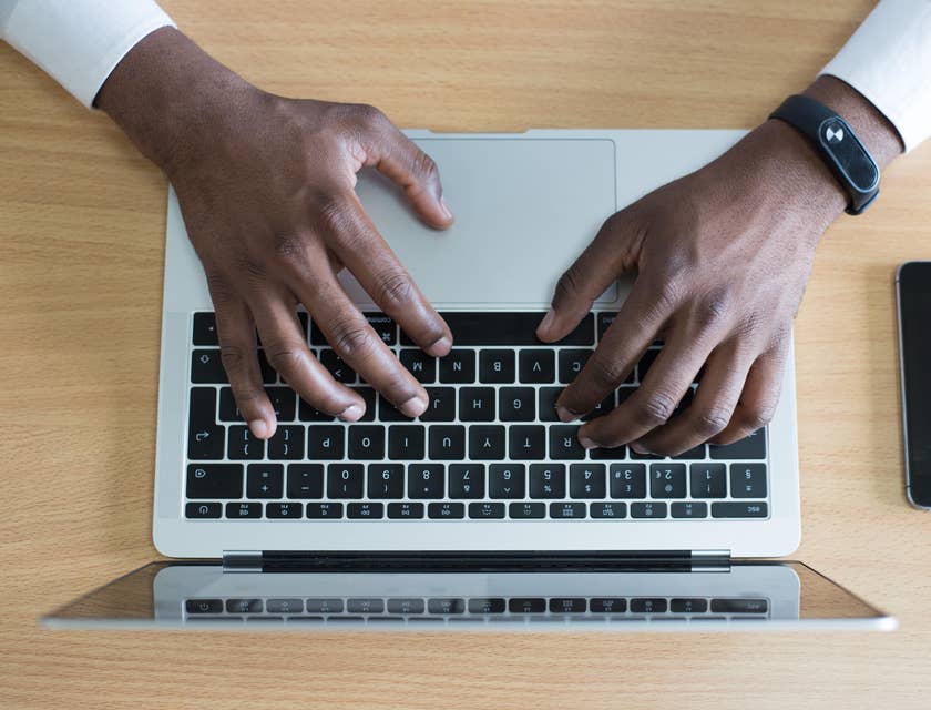 Person's hands on a MacBook writing a job description with an iPhone next to them.