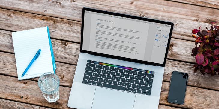 a laptop with a targeted resume on the screen on a wooden desk next to a notepad and glass of water
