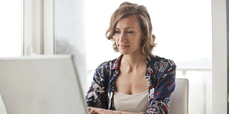 A woman in a blue floral top sitting while using a laptop.