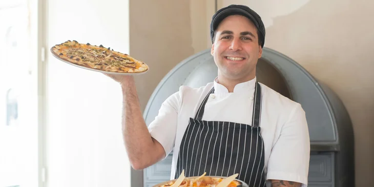 A chef holding pizzas to be baked.