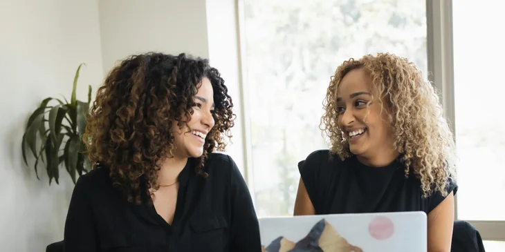 Two female coworkers smiling at each other while working.