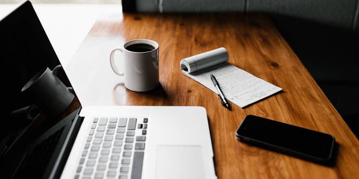 A laptop, phone, and notepad on a table ready to use to write a job posting template.