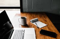 Un ordinateur portable, un téléphone et un bloc-notes sur une table prêts à être utilisés pour rédiger un modèle d'offre d'emploi.