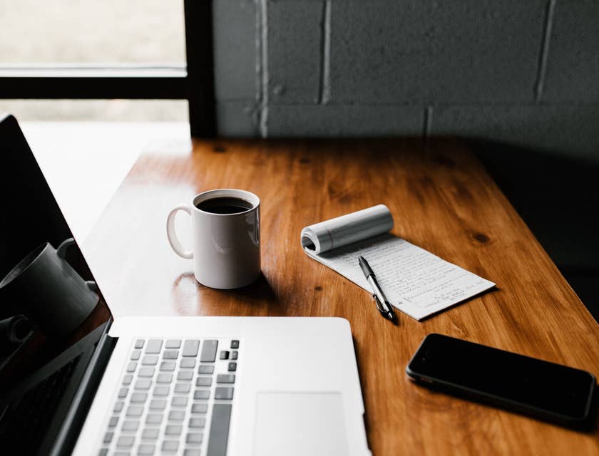 A laptop, phone, and notepad on a table ready to use to write a job posting template.