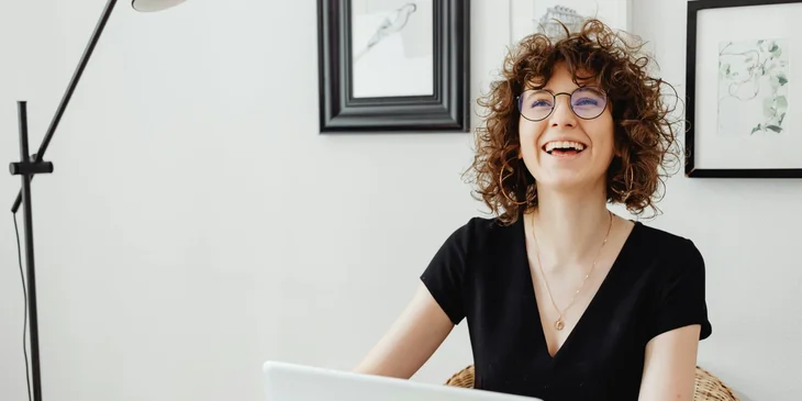 A cheerful woman sitting in front of a laptop.