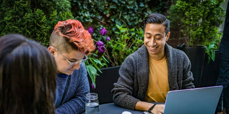 A man in orange crew-neck shirt using a laptop.