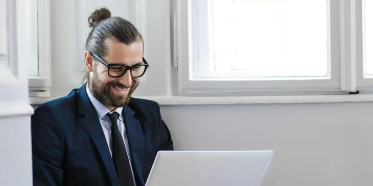 Un uomo che lavora al computer mentre sta seduto per terra con il computer sulle gambe.