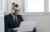 Un uomo che lavora al computer mentre sta seduto per terra con il computer sulle gambe.