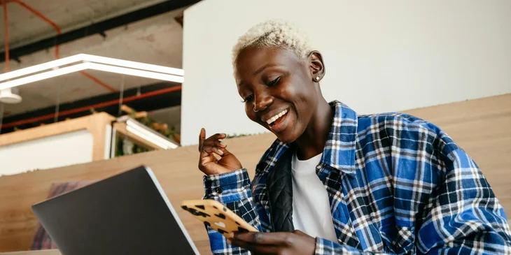A cheerful woman holding a phone and a laptop.