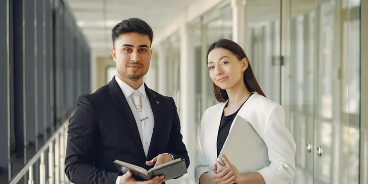 Two coworkers standing in an office hallway.