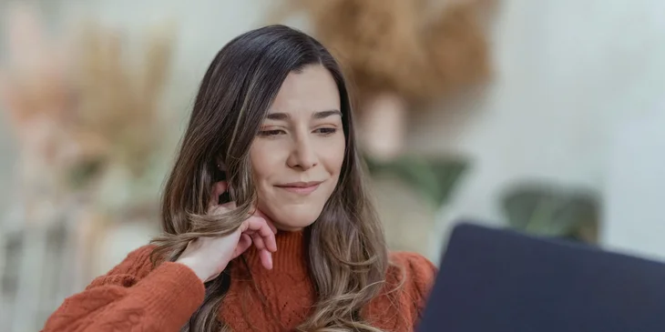 A woman smiling while working on a laptop.