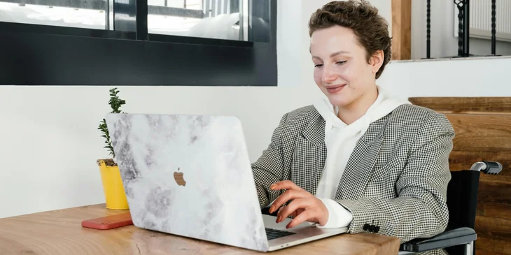 A woman in a wheelchair working on a laptop in a cafeteria.