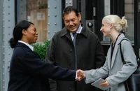 Drei lächelnde Menschen stehen vor einem Gebäude und lernen einander kennen.