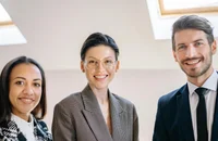 Drei Kollegen stehen lächelnd im Arbeitsplatz.